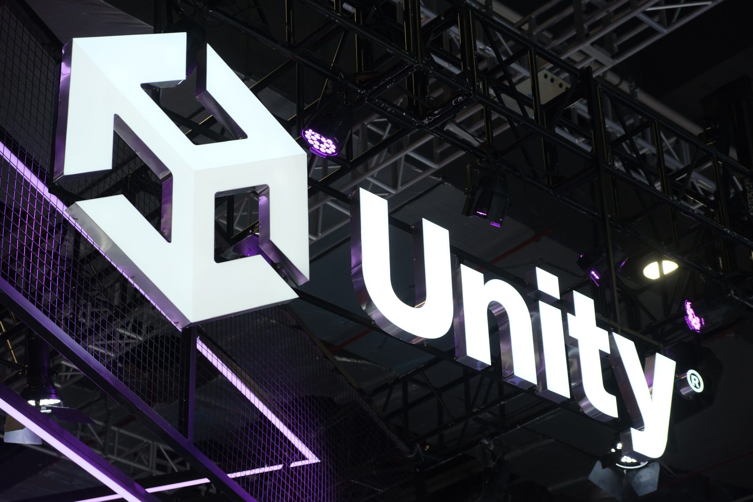 Das beleuchtete Logo von Unity, einer führenden Plattform für Game Development, hängt an einer Messestanddecke, umgeben von violetter Beleuchtung.