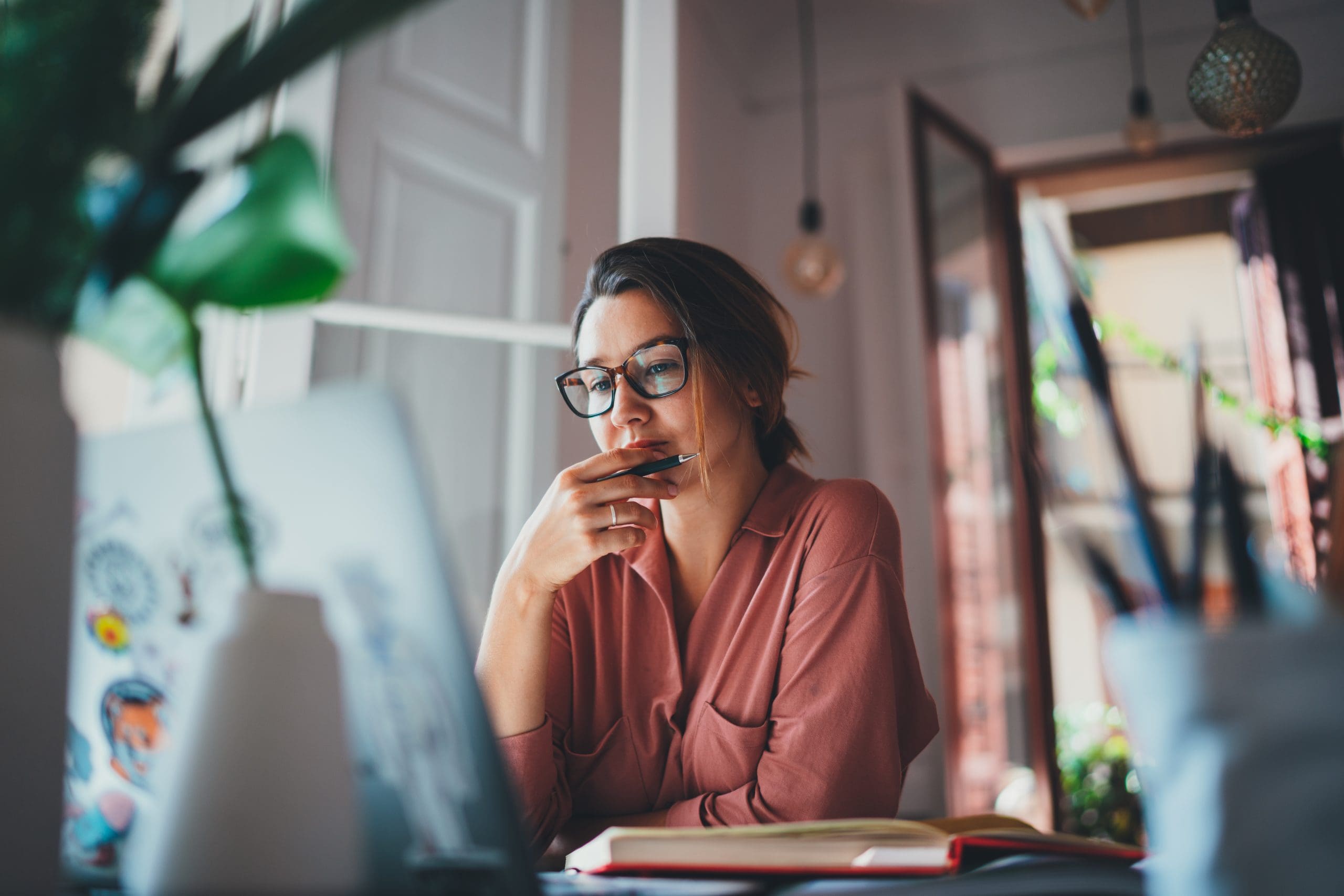 Eine nachdenkliche Frau mit Brille sitzt vor einem Laptop und notiert Strategien für SEO, konzentriert auf On-Page und Off-Page Optimierung.