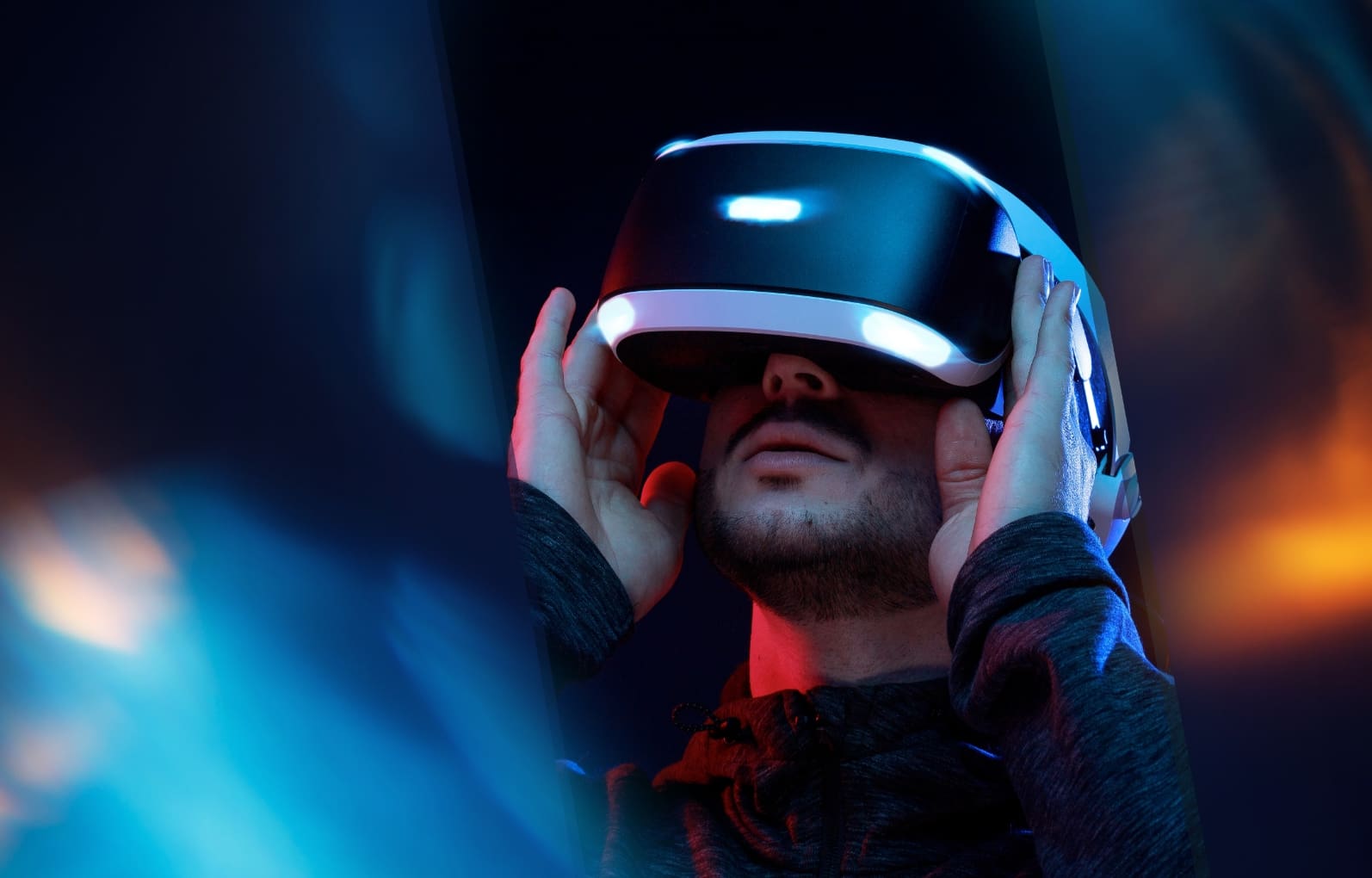 Ein Mann setzt ein Virtual Reality (VR) Headset auf, eingetaucht in eine Augmented Reality (AR)-Erfahrung, umgeben von farbigem Licht, das eine immersive VR/AR-Umgebung andeutet.